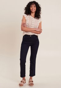 Lichtbeige kanten gebreide top met gegolfde randen, gecombineerd met marineblauwe skinnyjeans en tan platform sandalen. Eenvoudig, clean ontwerp.