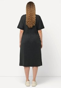Robe noire, longueur genou, à manches courtes et taille élastique. Dispose d'une texture lisse et d'ouverture sur les côtés pour faciliter le mouvement.
