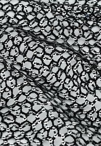 Tissu en dentelle noire avec des ornements circulaires en sequins disposés en motif géométrique à maille ouverte sur un fond clair.