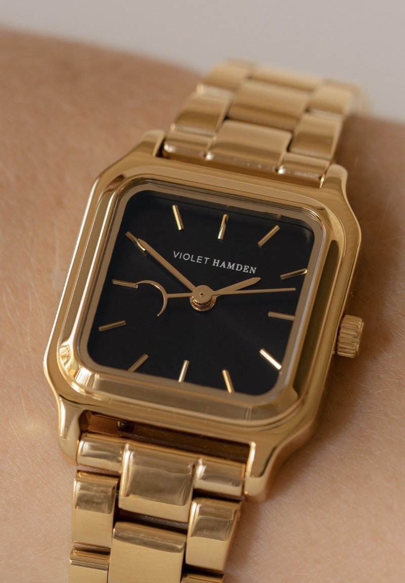 Goldfarbenes rechteckiges Armbanduhren mit einem schwarzen Zifferblatt, goldenen Stundenmarkierungen und einem einfachen Mondphasenanzeiger. Verfügt über ein verknüpftes Metallarmband.