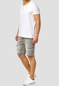 Witte T-shirt met korte mouwen en twee bruine knopen bij de hals, gecombineerd met lichtgrijze cargo shorts met zijzakken en een gestructureerde stof.