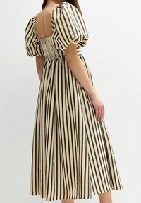 Raidallinen mekko beigen ja mustan sävyissä, jossa on puffihelma, rypytetty selkä ja polvipituinen hame, jossa on sivuaukot. Raskaampi kangas.
