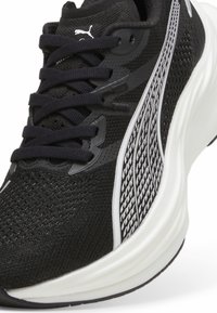 Zapatillas deportivas negras con parte superior de malla, acentos texturizados y una media suela blanca. Cintas y logo de Puma en blanco contrastante.
