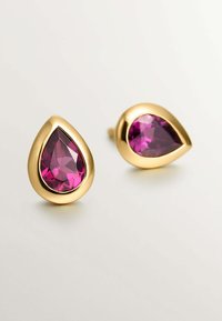 Los pendientes en forma de pera de color dorado presentan grandes piedras preciosas moradas facetadas, engastadas en un bisel suave y pulido que resalta su color vibrante.