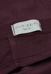 Bordeaux stof met een gladde textuur, voorzien van een wit etiket waarop "intimissimi Natural" staat. Zichtbare stiksels langs de randen.