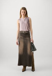 Top senza maniche di un leggero colore viola, dal taglio ampio, con scollo a V, abbinato a una lunga gonna di jeans marrone con una cintura larga e una fibbia argentata. Stivali marroni al ginocchio e una borsa nera strutturata completano l'outfit.