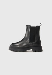 Zwarte leren Chelsea boot met dikke lugzool, elastische zijpanelen en een trekloop aan de achterkant, weergegeven in profiel op een witte achtergrond.