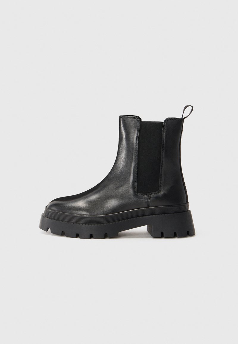 Zwarte leren Chelsea boot met dikke lugzool, elastische zijpanelen en een trekloop aan de achterkant, weergegeven in profiel op een witte achtergrond.