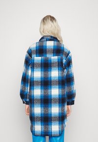 Camicia di flanella a quadri blu e nera con una vestibilità ampia, collo con risvolto e polsini con bottoni, caratterizzata da una texture morbida e da un design posteriore più lungo.