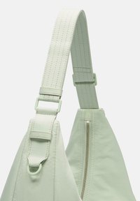 Borsa a spalla verde chiaro con una finitura liscia e texture. Dotata di una cinghia robusta, hardware regolabile e una tasca con zip.