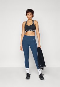 Crni sportski grudnjak s "Nike Pro" oznakom, u kombinaciji s tamnoplave tajice s bočnim džepovima. Nosie crne sportske cipele i bijele čarape.