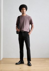 Tricou scurt cu mâneci maro, pantaloni negri, încălțăminte neagră și o geantă de umăr neagră. Material neted, croială dreaptă și detalii subtile.