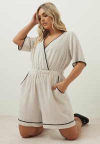 Ljusbeige linne romper med svart kant, med V-ringning, korta ärmar, elastisk midja och sidofickor.