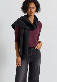 Mörkgrå scarf hängande över en vinröd långärmad topp; svarta vida jeans. Slät textur med ett subtilt rippat mönster på scarfen.