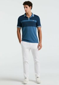 Navy blue polo shirt with striped collar and sleeves, featuring a textured panel design. Paired with white pants and white sneakers.
