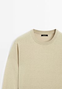 Pull beige col rond avec col côtelé et manches longues, en tissu tricoté doux, posé à plat sur un fond blanc.