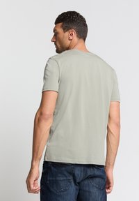 Lichtgroene t-shirt met korte mouwen en ronde hals, met een gladde textuur en een losse pasvorm, gedragen met donkere spijkerbroek.