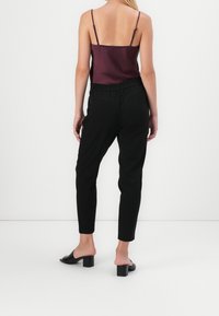 Pantalons noirs ajustés avec une taille élastique, associés à un caraco en satin bordeaux. Présente une coupe slim et un design longueur cheville.