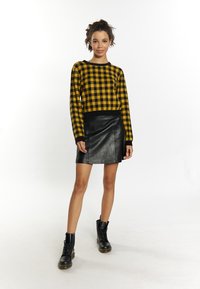Pullover a scacchi nero e giallo con maniche lunghe, abbinato a una gonna mini in pelle nera e stivali neri con lacci.