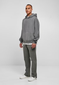 Felpa grigia oversize con tasca frontale, abbinata a pantaloni grigi nella stessa tonalità e sneakers bianche; realizzata in morbido misto cotone, vestibilità rilassata con polsini a coste.