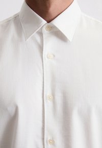 Witte blouse met een klassieke kraag, een gladde textuur en kunststof knopen langs de knoopsluiting. Eenvoudig en strak ontwerp.