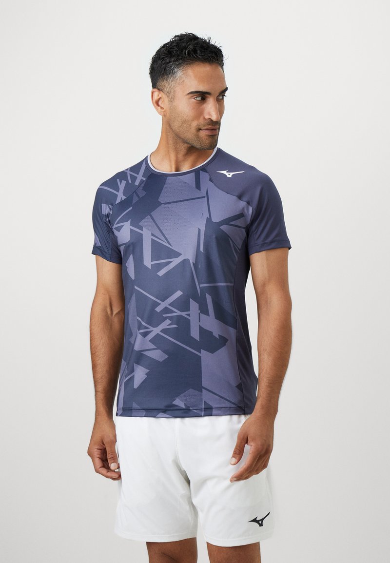 Tricou sport cu mânecă scurtă, de culoare bleumarin, cu modele geometrice, decolteu rotund și material respirabil. Purtați-l cu pantaloni scurți albi.