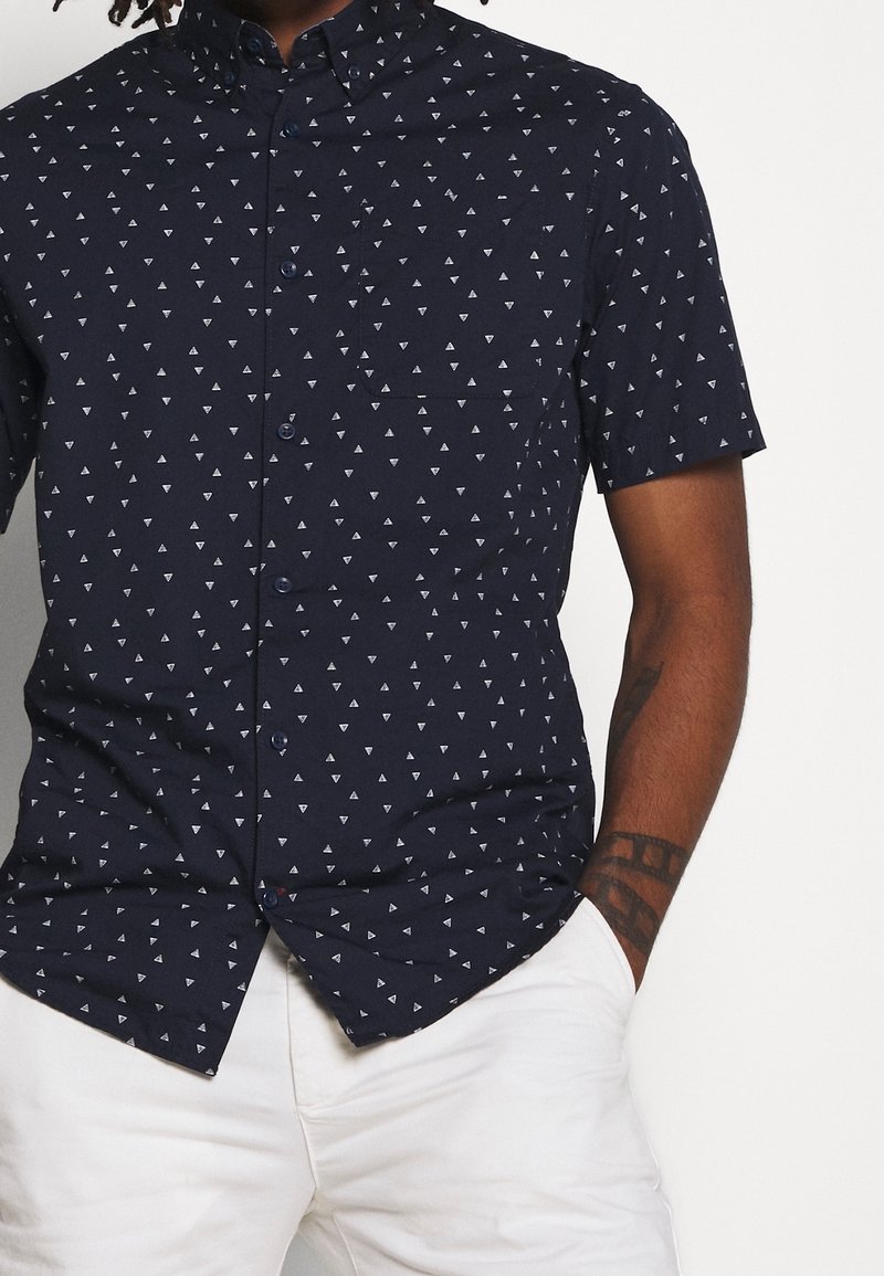Camicia a maniche corte navy con un motivo triangolare bianco, design con bottoni, colletto piccolo e taschino sul petto.