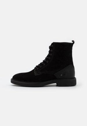 Bottines noires en suède avec un bout arrondi, un laçage à l'avant, un talon renforcé et des détails texturés sur le côté.