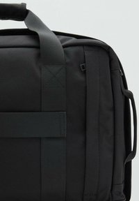 Sort stofpose med en tekstureret overflade, vandrette stropper og et solidt håndtag. Detaljer i et lignende mørkt materiale for et ensartet design.