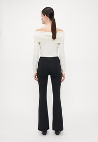 Crème off-the-shoulder top met lange mouwen, gecombineerd met aangesloten zwarte flared pants. Gladde textuur, geribbelde halslijn en hoge taille.