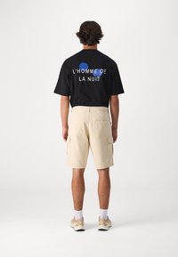 Černé tričko s nápisem "L'HOMME DE LA NUIT" v bílé a modré na zadní straně, spárované s béžovými cargo šortkami s bočními kapsami.