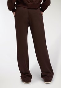 Pantaloni da jogging larghi e marroni in morbido tessuto, con tasche laterali e una texture liscia, dalla vestibilità comoda e un orlo pulito.