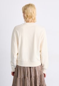 Krämfärgad sweatshirt med rund halsringning, långa ärmar och ribbad nederkant, i kombination med en rutigt lager-på-lager kjol i bruna och beige toner.