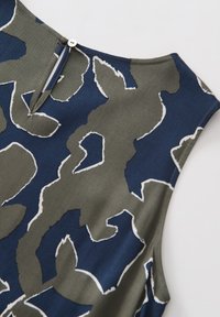 Navy and olive green patterned fabric featuring abstract shapes, with a white outline; includes a small button closure at the back.