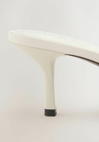 Chaussure blanche à talon haut avec un talon fin et une pointe noire sur un fond neutre, vue de profil.