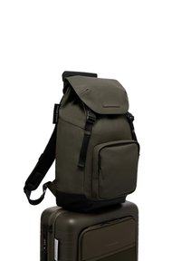 Sac à dos vert olive avec une fermeture enroulable, des bretelles réglables, une poche avant et une texture lisse, reposant sur une valise assortie.