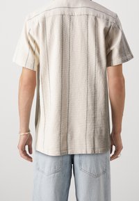 Košile s krátkým rukávem v off-white texturované tkanině s vertikálními modrými pruhy, s uvolněným střihem a rovný lem.