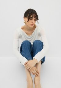 Vit långärmad topp med rundad halsringning, kombinerad med blå denimjeans. Jeansen är något avkortade med fransat nederkant.