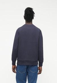 Tmavě modrá mikina s dlouhými rukávy, žebrovaným límcem a manžetami a rovnými lemy. Pohled zezadu ukazuje hladký, texturovaný povrch.