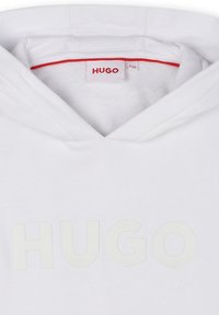Hoodie blanc avec une finition texturée, arborant un grand logo "HUGO" de couleur claire. Design à capuche et accent rouge sur le col intérieur.