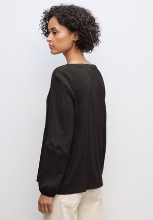 Svart, texturerad blus med långa ärmar och rund halsringning. Har detaljerad sömnad på ärmarna och en avslappnad passform.