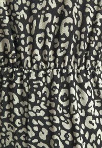 Tissu imprimé léopard noir et beige avec une couture froncée créant de légers plis et une texture sur la matière.