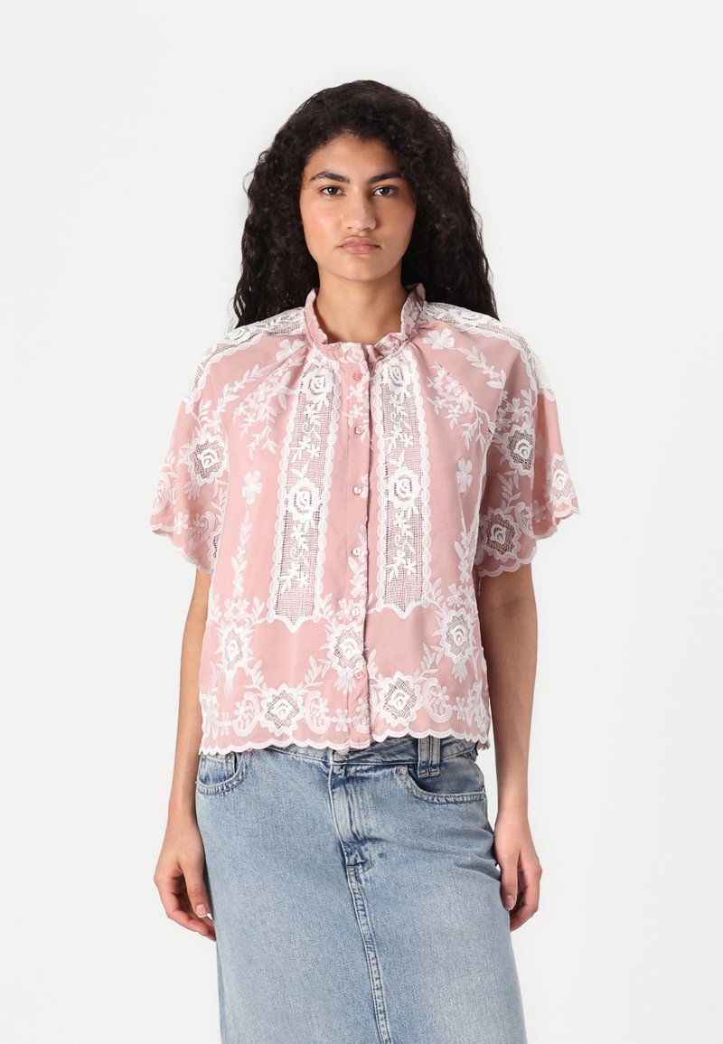 Blusa in pizzo rosa con maniche corte, intricati ricami floreali, orlo scallop, scollatura rotonda e chiusura anteriore con bottoni.