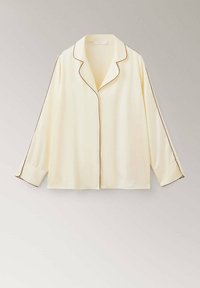 Haut de pyjama en soie couleur crème à manches longues avec passepoil marron foncé le long du col, du devant, des manches et des poignets, présenté sur fond uni.