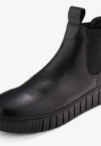 Bottine Chelsea noire avec tige en cuir lisse, panneaux élastiques sur les côtés et semelle en caoutchouc striée. Dispose d'une languette au niveau du talon.