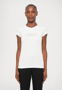 Biela bavlnená tričko s okrúhlym výstrihom a kr�átkymi rukávmi, s jemným ružovým logom "ARMANI EXCHANGE" na prednej strane.