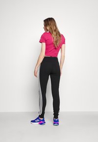 Rosa Cropped T-Shirt mit kurzen Ärmeln, kombiniert mit schwarzen Leggings mit weißen Streifen. Getragen mit blauen und rosa SportSchuhen.