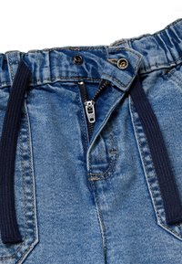 Pantalones de mezclilla con cintura elástica, de color azul, con cierre de cremallera y botón, que presentan un cordón de color marino y detalles de costura expuesta.