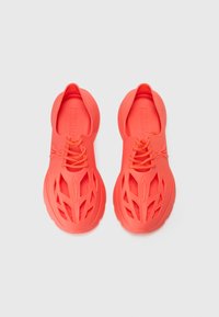 Lyse korallfargede sneakers laget av gummi, med utskjærte design, teksturerte mønstre og sentral snøring med tjukke såler.