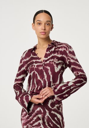 Bordeaux gemusterde blouse met een knoopsluiting aan de voorkant, lange mouwen en een kraag. Heeft een textuurstof met golvende, contrasterende zilveren accenten.